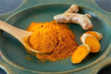 Turmeric root and turmeric powder on wooden background