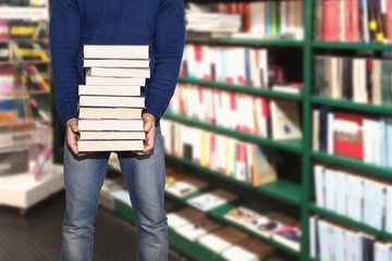 uomo in libreria che acquista libri tenendoli in mano tra corridoio e scaffali