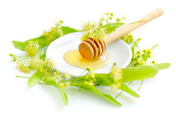Honey dipper with honey with flowers of linden on white saucer