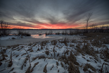 Sunset blazes away in orange and red over a lake and snow covered sedge wetland.