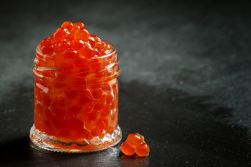 Red caviar in a glass jar on black stone background, selective f