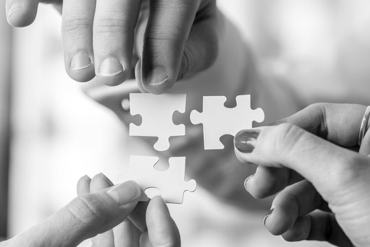 Black and white image of three people holding puzzle pieces to m
