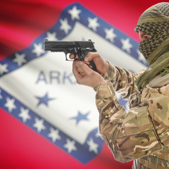 Side view of man in camouflage holding gun against flag of Arkansas