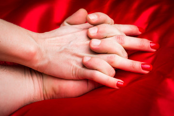 Young couple holding hands sensually on red silk bed.