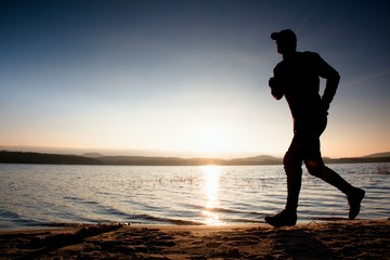 Fototapeta na wymiar Running man on beach. Sportsman run in baseball cap, jogging guy during the sunrise