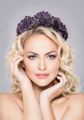 Close-up of young, sensual woman wearing purple flower alike coronet over grey background.