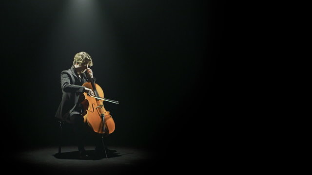 Cellist is playing his cello alone on stage   