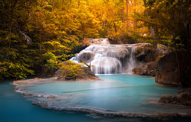 Fototapeta na wymiar Orange autumn leaves of wild dense forest and scenic waterfall falls in natural blue water pond