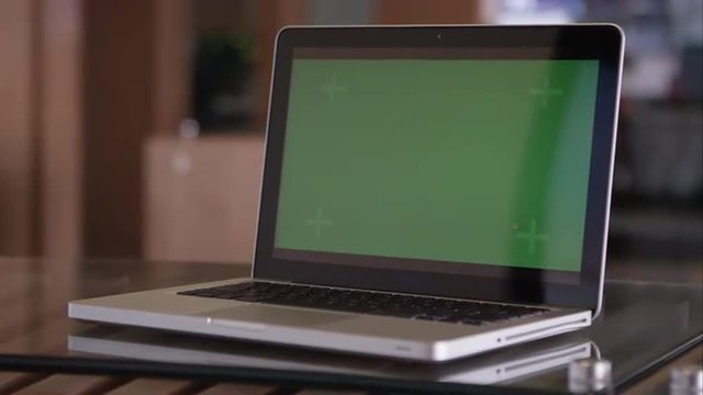 Panning shot of laptop with green screen on table.
