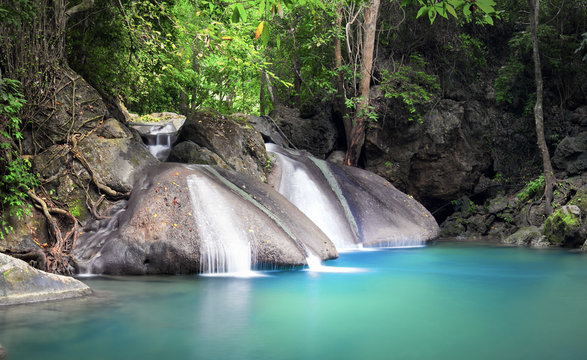 Peaceful and relaxing landscape background of tropical forest with small beautiful waterfall flowing from wet stones and rocks and falling in blue water lake