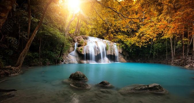 Waterfall in autumn forest with bright sun light and small natural lake with clear blue water