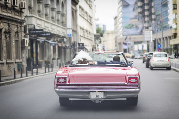A newlywed married couple is driving a convertible retro car in