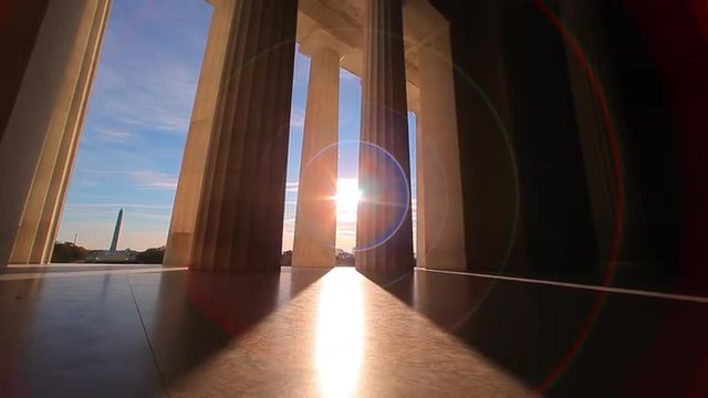 Lincoln Memorial, tracking shot of giant pillars with lens flare and blue cloudy sky, early morning.