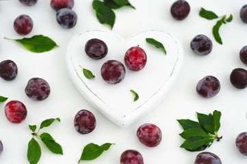 White wooden heart and ripe juicy plums on a white background