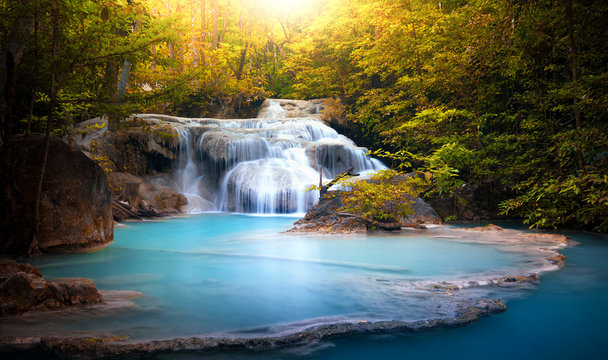 Sunlight through tree leaves lights beautiful waterfall in forest