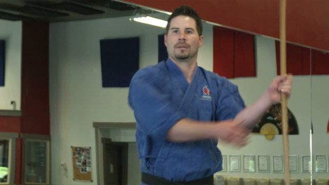 Man in karate gear practicing bow staff weapon moves
