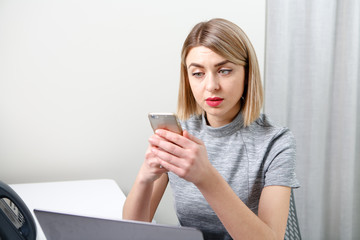 Young pretty business woman with mobile phone sitting at her workplace in office