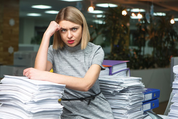 Office businesswoman at her desk full of documents, showing an overwhelmed expression
