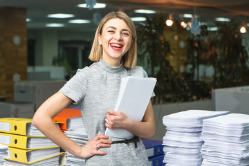 Smiling young woman holds the stack of paper in the office