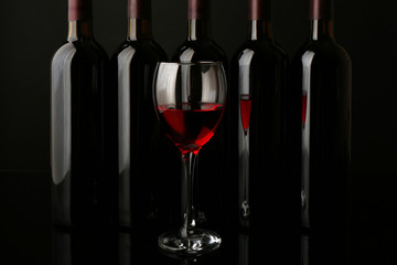Red wine glass against bottles in a row on black background, close up