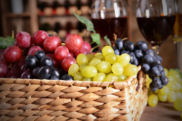Grape in wicker box on a table on wine bottles background