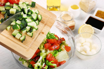 Female hands adding vegetables  into bowl with salad, close-up