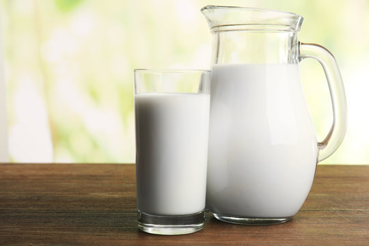 Milk in jar and in glass on table on blurred natural background
