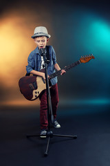 Naklejka premium Little boy playing guitar and singing with microphone on a dark lighted background