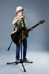 Naklejka premium Little boy playing guitar and singing with microphone on grey background