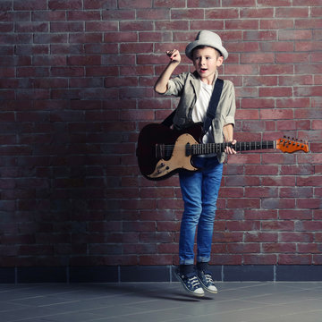 Little boy playing guitar on a brick wall background