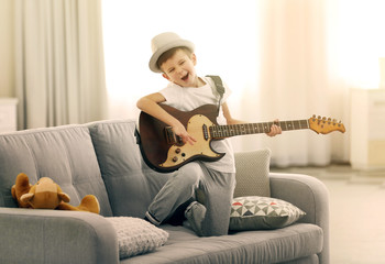 Obraz premium Little boy playing guitar on a sofa at home