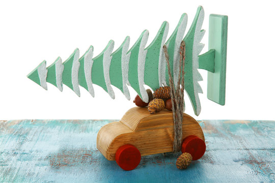 Wooden toy car with Christmas tree and cones on a table over white background