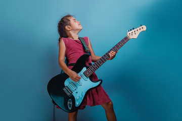 Obraz na płótnie Canvas Girl European appearance ten years playing guitar on a blue ba