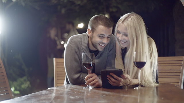 Couple smiles with wine uses tablet  slow motion  