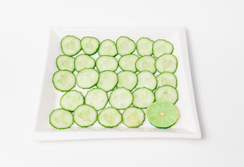 Closeup view of fresh sliced green cucumbers with lime piece in ceramic plate isolated on white background