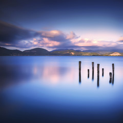 Wooden pier or jetty remains on a blue lake sunset and sky refle