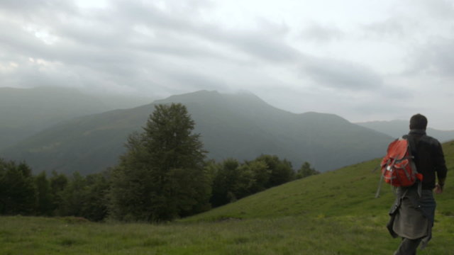Man is walking outdoor on mountain path in overcast day   
