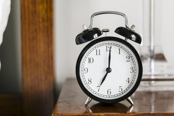 Black alarm clock showing 7 o'clock on bedside table