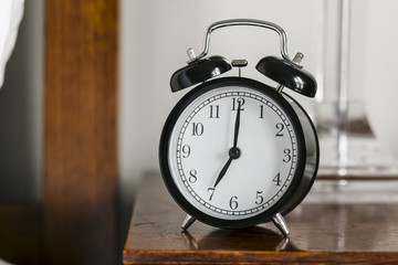 Black alarm clock showing 7 o'clock on bedside table