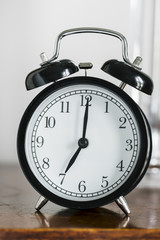 Black alarm clock showing 7 o'clock on bedside table