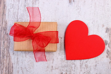 Wrapped gift for Valentines day and red heart on old wooden table