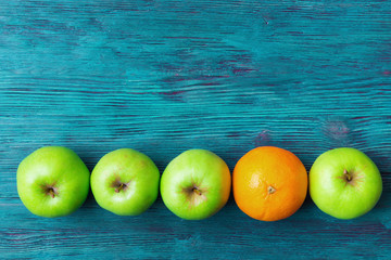 Green apples and one orange over rustic wooden background