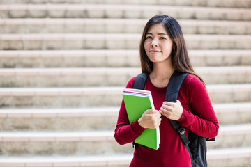 Smiling college student sitting on staircase and studying with b