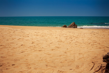 view of beach with stone against azure sea with foamy wave surf