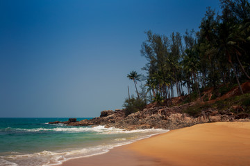 foamy wave surf strikes against rocky bank by beach against sky