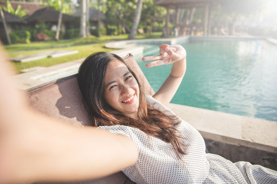 woman relaxing next to the pool and taking selfie