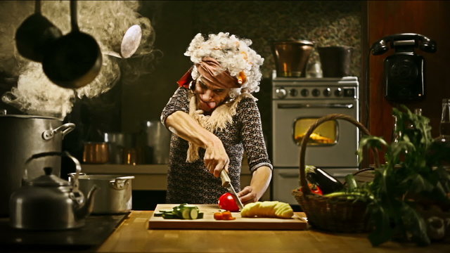 Funny senior housewife is cutting vegetables in an old kitchen   