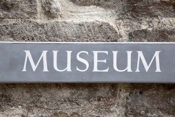 Grey Wooden Museum Sign on Stone Wall