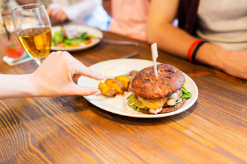close up of friends hands sharing burger at bar