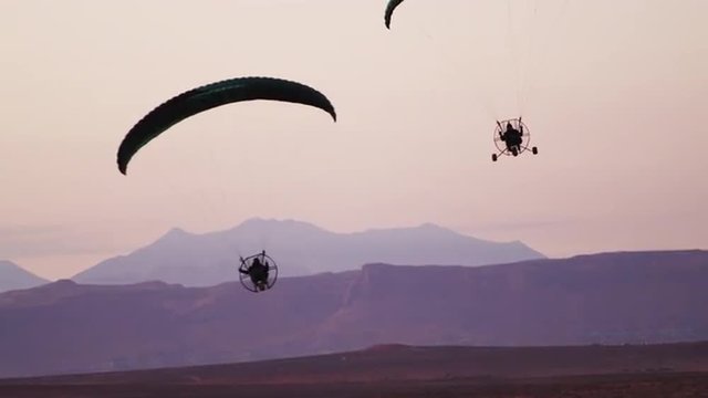 Pan shot of two powered paragliders at dusk.